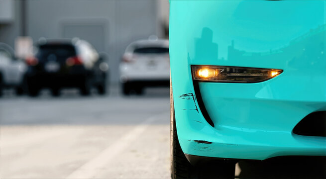 Scratched turquoise car bumper with glowing amber signal light. Minor parking accident and vehicle damage. Close up of paint scuffs on front fender