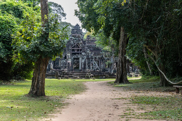 Fototapeta premium The ancient stone ruins of Banteay Kdei temple in Siem Reap, Cambodia, are overgrown with lush green jungle foliage, showcasing its historical significance.