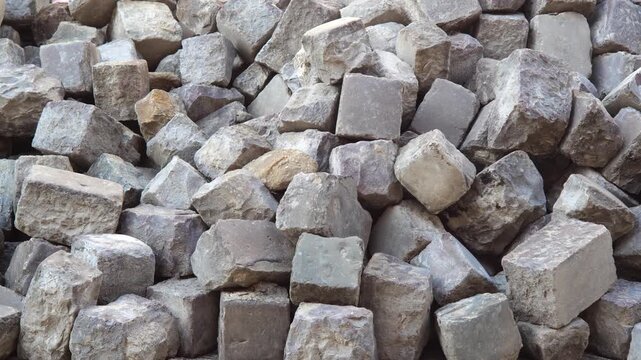 Slow pan across a large heap of reclaimed gray paving stones and rough rectangular cobblestones, construction demolition rubble background textured masonry blocks, building material waste, no people