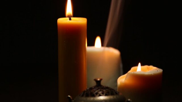 Three magic Christmas wax candle flames calm burning in home in white smoke from incense aroma stick on black dark background with copy space. Closeup yoga, spa, wellness, relaxation. No people