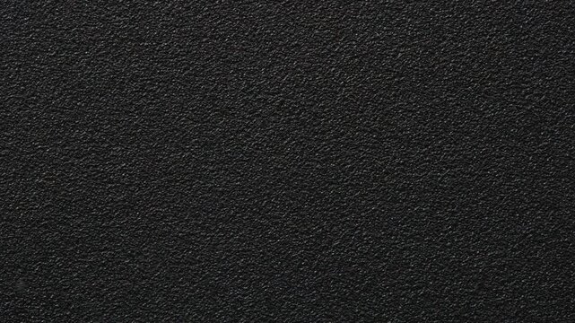 Slow pan across dark black textured plastic surface, full frame macro background of rough grained casing material with subtle highlights, minimal abstract backdrop with copy space, no people