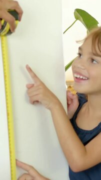 Vertical video: Pointing kid navy top urging adult lining yellow tape marking home wall, copy space