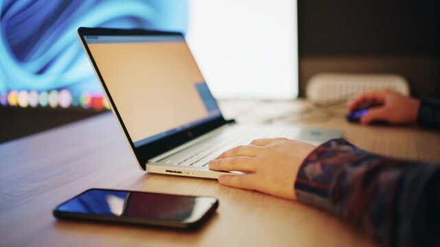 Close up of person hands working on laptop computer while using mouse on wooden desk.