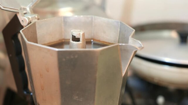A slow zoom in reveals a steaming moka pot on the stove. Hot espresso. Black coffee. Steam rising from a coffee maker. An Italian coffee maker on a stove. POV: preparing coffee. Making coffee. 