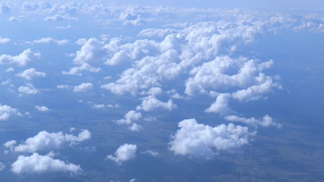 Aerial view of fluffy white cumulus clouds over a hazy blue landscape from an airplane, peaceful high altitude cloudscape background with soft daylight, calm travel and freedom concept, no people