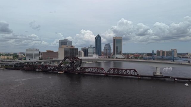 Aerial view of the downtown skyline, the FEC railroad bridge, and the Acosta Bridge over the St. Johns River under a cloudy sky in Jacksonville, Florida, United States.
