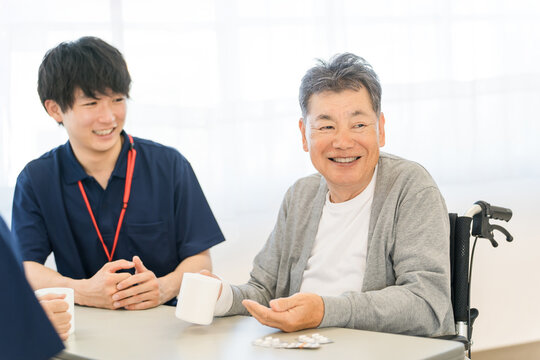 A smiling senior man taking medication at a nursing home/elderly care facility, with a male caregiver.