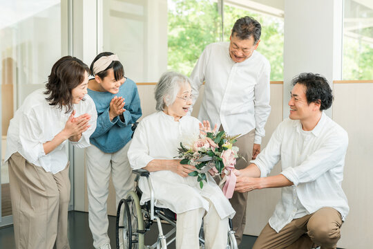 A three-generation family visits their grandmother in a care facility and presents her with a bouquet of flowers as a get-well gift.