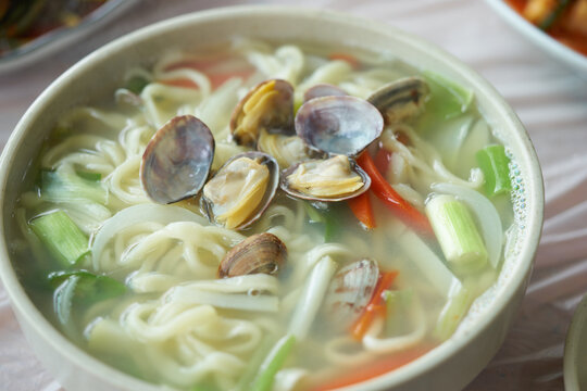 A documentary series captures local fishermen harvesting Manila clams on a vast tidal mudflat in Yeongheungdo, South Korea. The final image features a steaming bowl of traditional clam noodle soup.