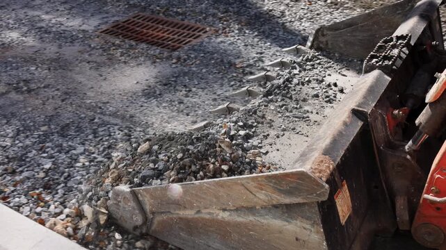 Tractor machine moves gravel on construction site with stones scattered on ground during road repairs
