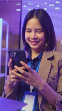 Smiling young Asian businesswoman using smartphone while wearing headset in office.