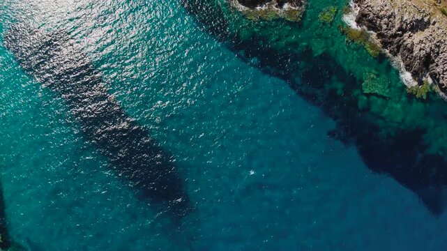 Aerial Drone View of Rocky Coastline and Crystal Clear Turquoise Sea Near Voidokilia Beach Greece With Sun Reflections and Underwater Reef Patterns in Mediterranean Waters
