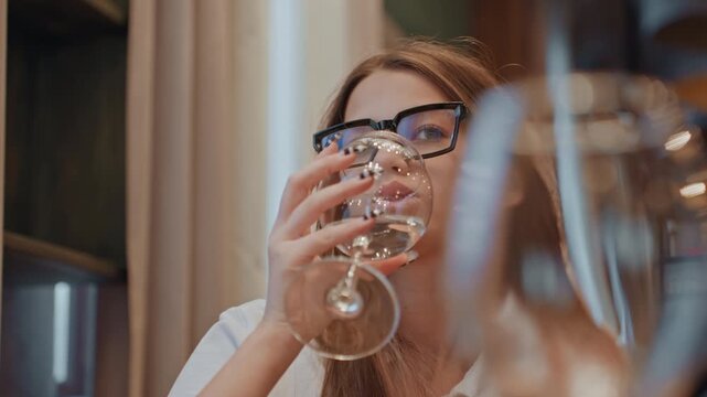 Closeup wine glass caucasian woman sipping. Intimate restaurant moment with young caucasian woman editor pausing between sips, droplets on glass stem, prescription glasses slipping, eyes closed