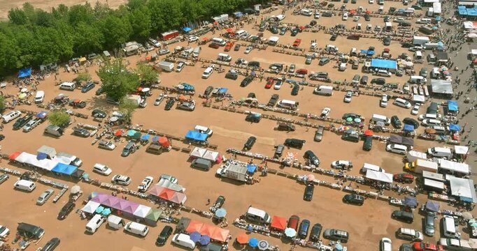 Many people walk around an open air flea market filled with tents cars vendors sell goods as shoppers busy atmosphere