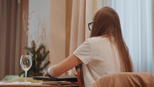 Young woman using laptop at table, checking screen and audio before online meeting presenter and remote worker actions include adjusting camera, testing microphone, logging in and taking notes