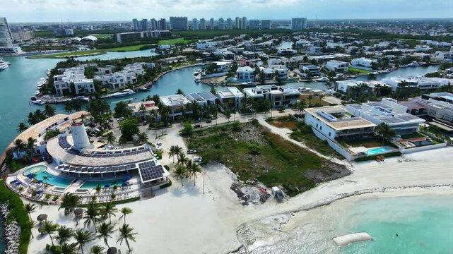 Aerial view tracking right over Puerto Cancun, Mexico. Smooth 4K 60fps drone shot showcasing luxury waterfront villas, private boat canals, upscale beach clubs, and turquoise sea.