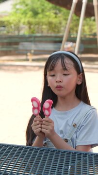 Young Asian Girl Eating Butterfly Shaped Ice Cream Popsicle in Park