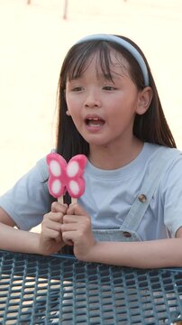 Young Asian Girl Eating a Butterfly Shaped Popsicle in a Park