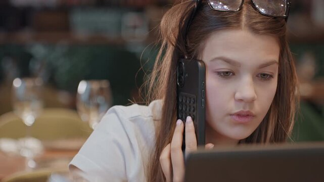 Focused caucasian woman on phone at restaurant table with laptop, sunglasses perched on head, alternating expressions of concentration, irritation and relief while negotiating project details