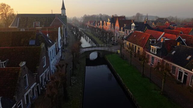 Aerial view of the historic canal and traditional gabled houses during a misty sunrise in Sloten, Friesland, Netherlands.