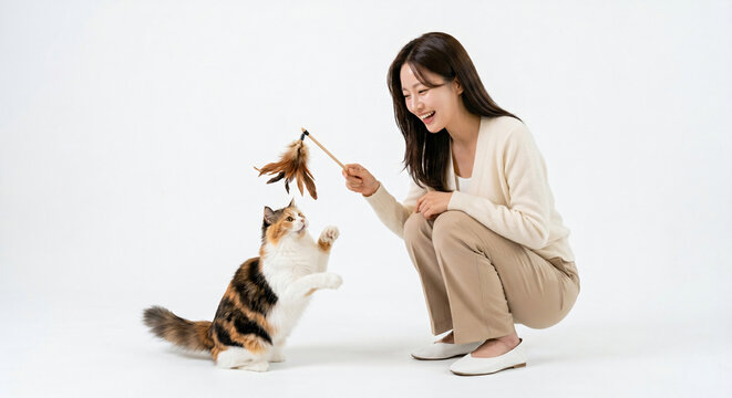 A happy woman playing with her playful calico cat on a white background, enjoying a fun moment