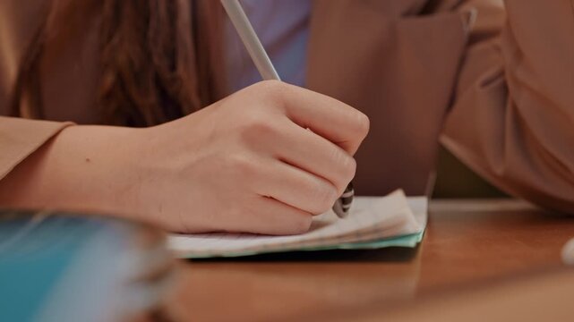 Hand writing in notebook at wooden table, pen nib gliding across paper, entrepreneur drafting plan and notes, contracts and agenda nearby, steady wrist, focused detail, productivity mood