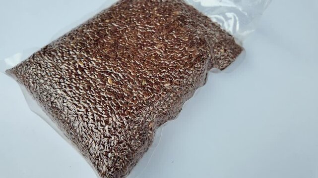 High angle close up of healthy brown flaxseed sealed tightly inside a clear transparent plastic pouch packaging for retail market sale.