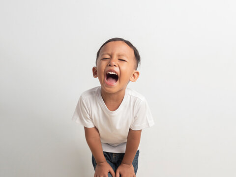 Adorable young asian boy wearing a simple white shirt showing a wide happy toothy smile while looking directly at the camera in this bright studio portrait photograph for your project