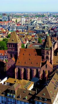 Vertical video. Strasbourg, France. St. Thomas Church, a Romanesque and Gothic hall church with a single tower and red sandstone facade, seen from a high aerial perspective above the historic city ce