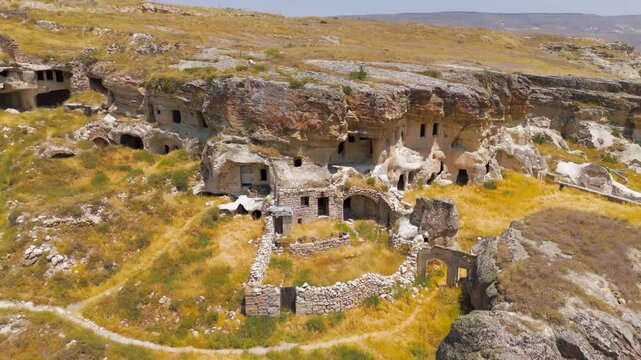 Urgup, Nevsehir, Turkey. Abandoned rock dwellings and cave houses carved into volcanic tuff cliffs, aerial drone view transitioning from close-up stone fence to wide panoramic landscape. Aerial View