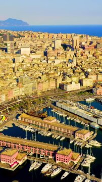 Vertical video. Genoa, Italy. Drone footage of Porto Antico with the glass Biosphere sphere, Bigo lift, and marina yachts against the Ligurian Sea under clear summer skies. Drone footage. Rich colors