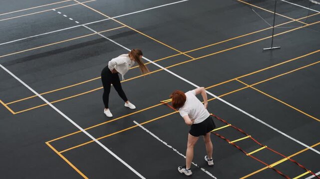 Intense badminton agility ladder training, performance coach pushing player through quick step drills and bursts, energetic tension and concentrated effort, visible court grid and training markers