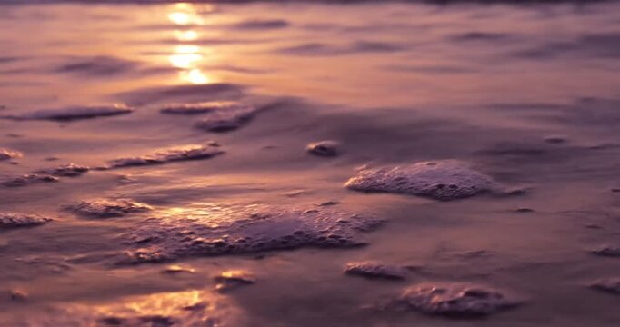 Serene sunset over gentle ocean waves, reflecting golden light with soft foam bubbles