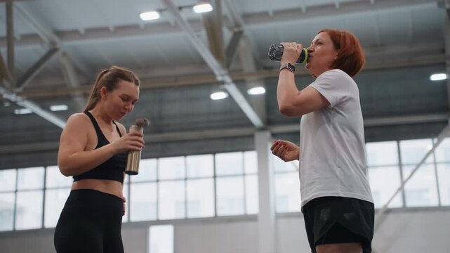 White athletes drinking water after intense badminton rally on indoor court, bottles raised overhead, expressive gestures and mutual encouragement, sweat and focused recovery between drills
