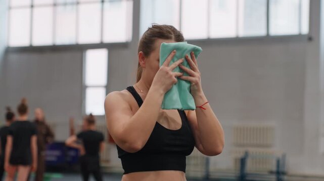 Midcourt caucasian athlete holding towel and steadying breath on indoor badminton court, teammates and coaches blurred in background, preparing mentally for next rally with focused ritual and calm