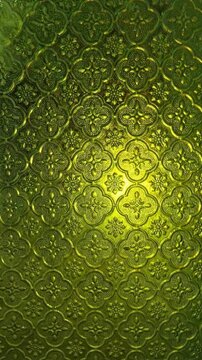 Textured green glass with an intricate floral pattern, illuminated from behind, creates an abstract and opulent decorative background.