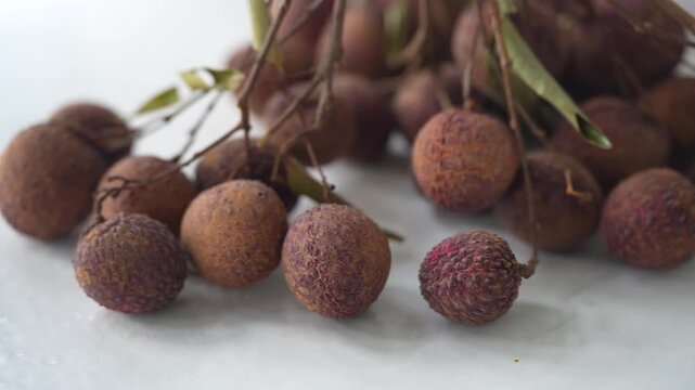 Overripe lychees with wrinkled, drying skins clustered on their branches, showing signs of aging and natural deterioration before spoilage