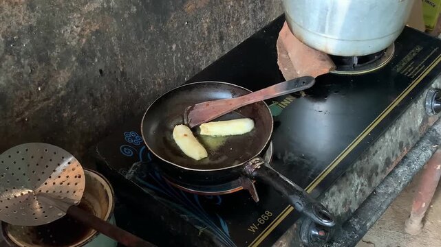 Person Cooking Sliced Bananas in a Frying Pan on a Stove.