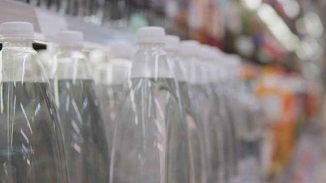 Hand checking bottled water label and cap, closeup inspection in supermarket aisle, focus on barcode and packaging, shopper evaluating quality and sustainability, muted background with soft store