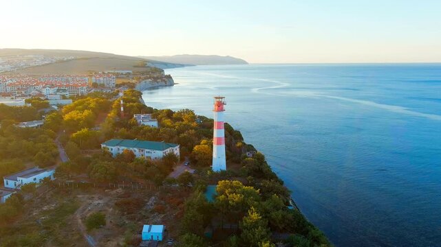 Gelendzhik, Russia. The red-and-white striped lighthouse on Cape Tolstoy, a tall octagonal tower rising from dense greenery above the Black Sea cliffs, Drone footage at golden hour. Drone footage, Po