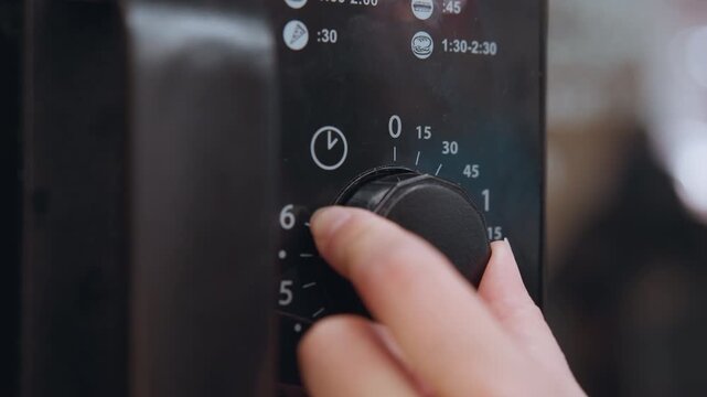 Closeup microwave dial with numeric markings and textured knob attentive finger nudges minute increments, black panel shows white numerals, shallow depth of field emphasizes tactile control