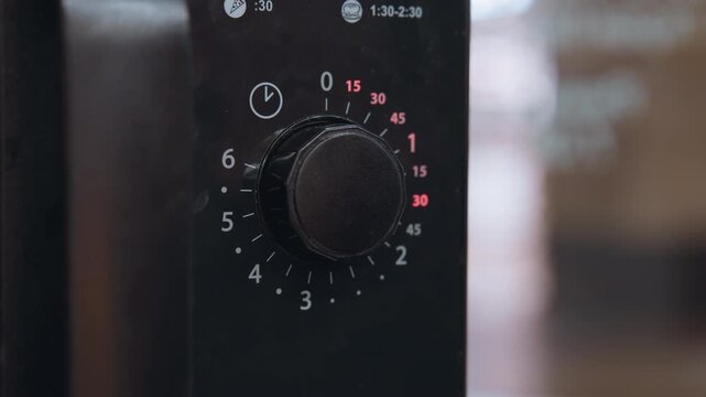 Microwave timer dial glowing red numbers while hand sets countdown textured knob rotated toward fifteen minutes, glossy black control panel, commercial kitchen vibe with focused prep and precise