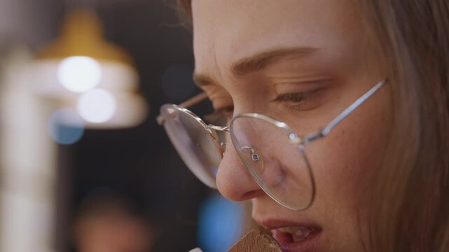 Closeup of distressed woman with reflective tears and background lighting effects. Expressive female image depicting vulnerability and emotional intensity amidst blurred cafe ambiance