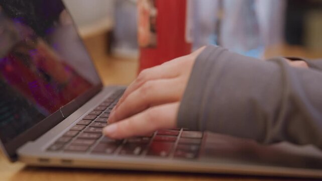 Closeup hands typing laptop keyboard, focused freelance work or student study session at wooden table with coffee, hoodie sleeves visible, quick precise keystrokes and screen glow create concentrated
