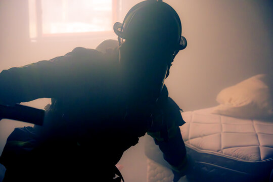 Silhouette of a firefighter performing a search for victims in a smoke filled room and sun shining in through a window in the background over his right shoulder. 