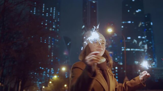 White woman holding sparklers in city. Nighttime street scene bundled in coat and beanie with glasses, smiling as sparks fly against neonlit skyscrapers and bokeh background, candid tourist portrait