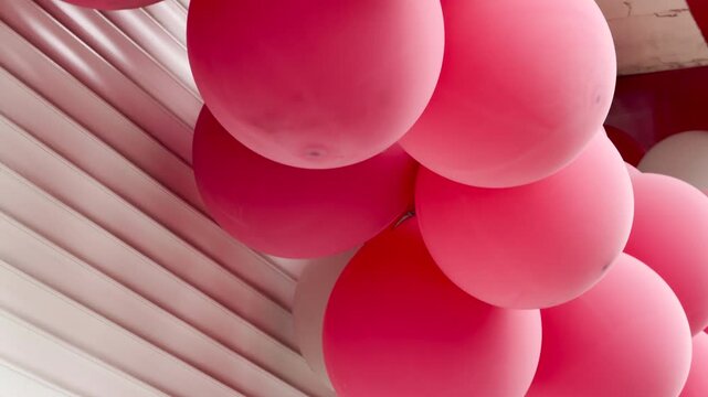 A thick cluster of pink and white latex balloons hangs arranged in a festive garland. The colorful decorations are positioned directly against a white, ribbed metal roller shutter door.