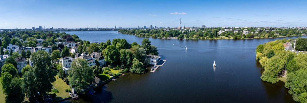 Aerial view of the Aussenalster lake with sailboats on the water, lush green trees, and the city skyline under a clear blue sky in Hamburg, Hamburg, Germany.