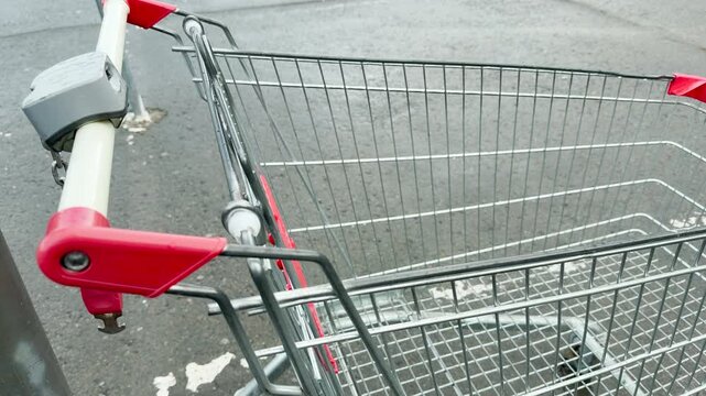 An empty wire shopping trolley sits parked on a damp pavement surface. The ambient environment carries the faint, distant, low-frequency hum of city traffic.