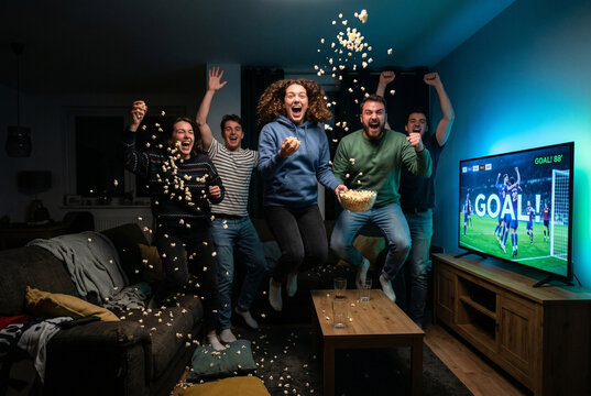 Excited friends cheering and throwing popcorn watching football match